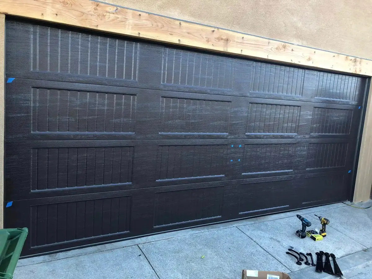 Dark carriage-style garage door with recessed panels and a wooden header