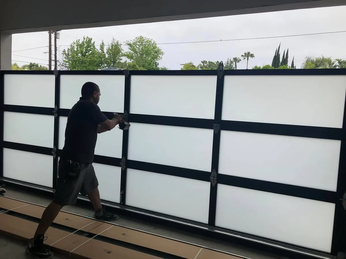 Full-view garage door panels with black frames and glass being installed